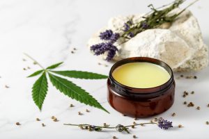 Composition with cannabis wax salve or cream with lavender extract, flowers, hemp leaves seeds. on marble background with copy space