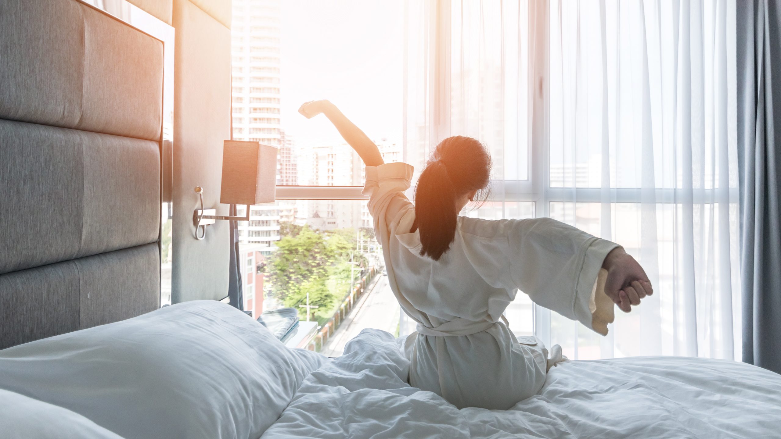 Hotel room comfort with good sleep easy relaxation lifestyle of Asian girl on bed have a nice day morning waking up, taking some rest, lazily relaxing in guest bedroom in city hotel